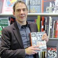 Volker Petri steht vor dem Comic-Regal, in seinen Händen die Graphic Novel "Packeis"