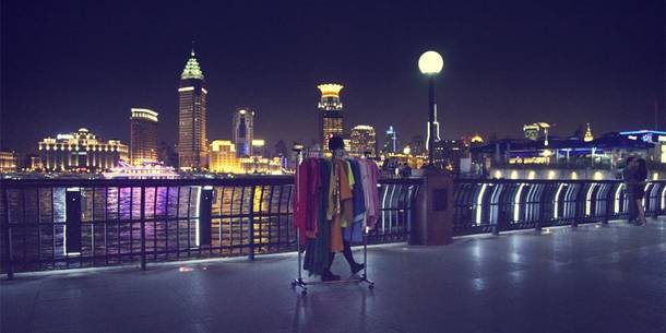 Foto der Performance "Mini View": Xiao Ke unterwegs mit Kleiderständer, im Hintergrund die Skyline Shanghais